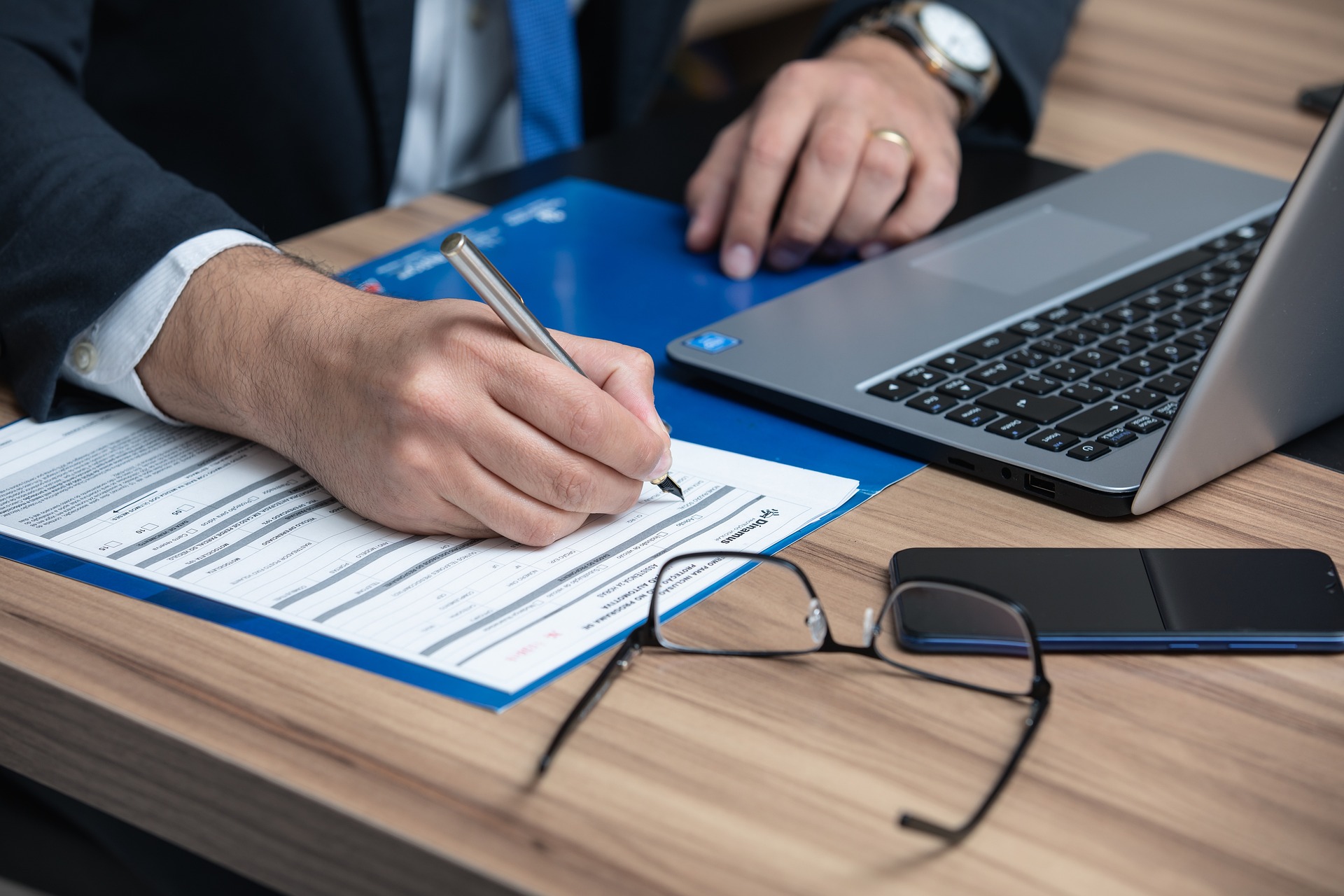 Business Transaction - Guy writing contract with laptop and glasses.